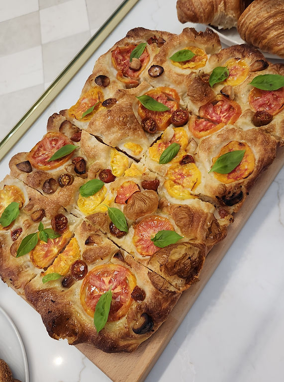 Focaccia bread with tomatoes and basil leaves on a wooden board at Runcible Spoon Bakery